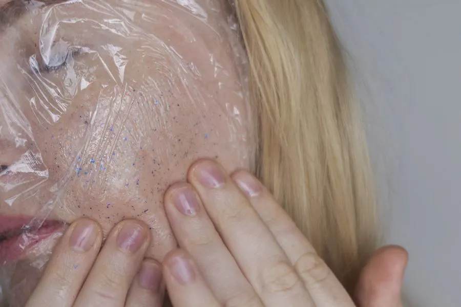 A girl with glitter on her cheek and plastic wrap overtop.